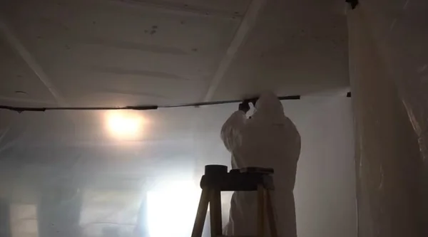 Mold remediation technician working inside a plastic-sheeted basement containment