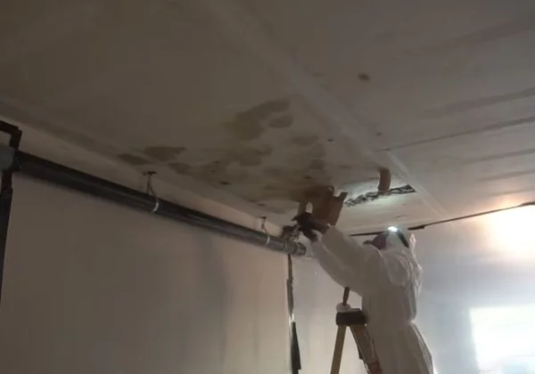 Technician in a protective suit working on a mold-damaged ceiling inside plastic containment
